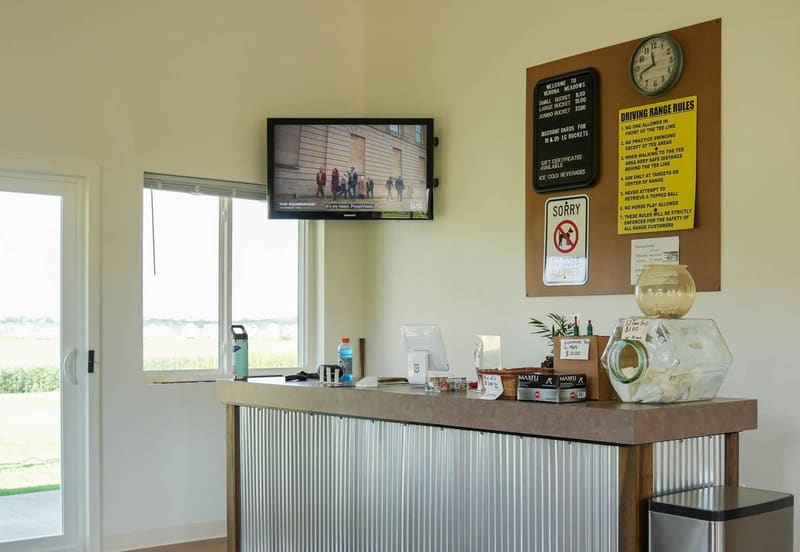 The counter inside the new clubhouse, with a corrugated-steel front, price board, and driving range rules on the wall