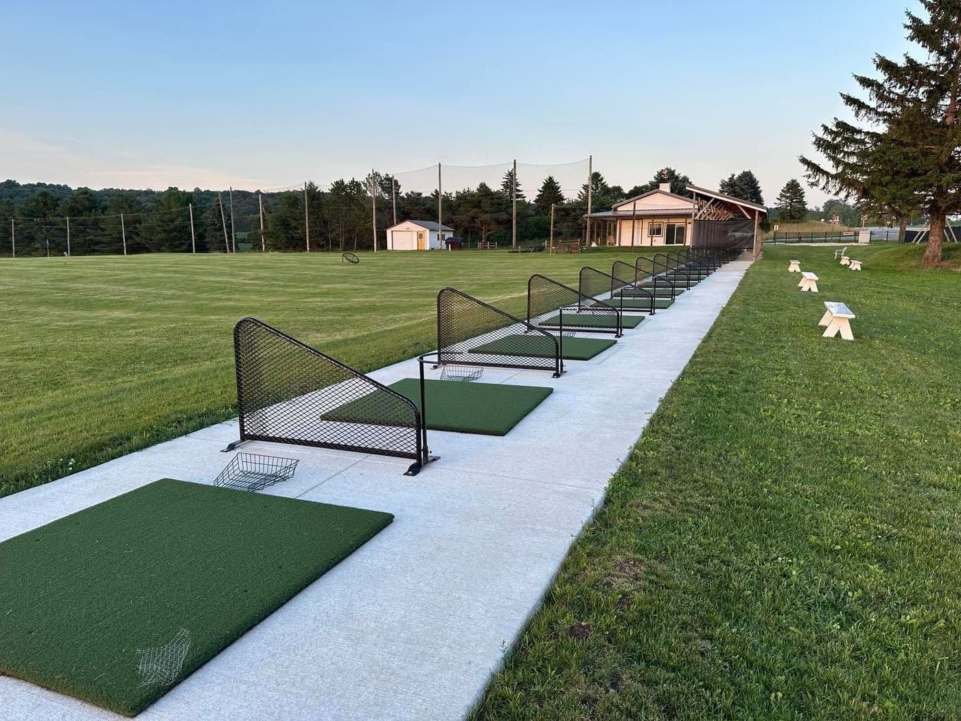 Golden-hour view down the tee line at Verona Meadows, with the covered hitting bays on the left and the sun setting over the range