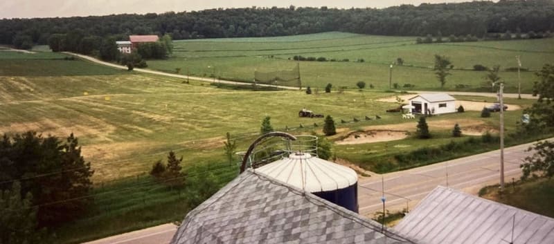 A mid-1990s photo of the driving range taken from the top of the farm silo, with the original shop building and rolling fields beyond