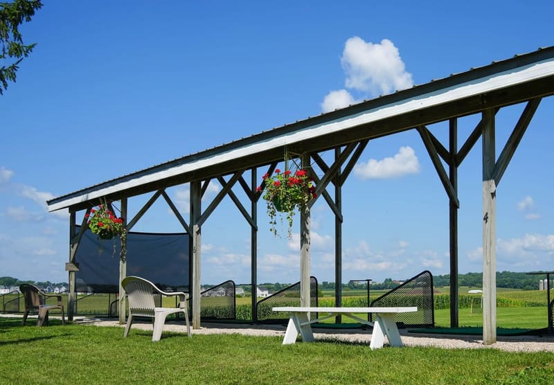 The covered pavilion bays with hanging geranium baskets, benches, and mats looking out over the range